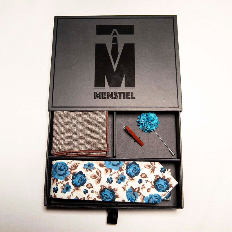 top view of chicory set in gift box with top - a men's accessories set - The earthy, wood tie bar along with the wool pocket square give rise to the bright, light blue flowers on the lapel pin and the floral tie