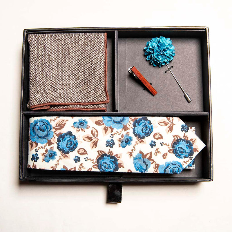 top view of chicory set in box - a men's accessories set - The earthy, wood tie bar along with the wool pocket square give rise to the bright, light blue flowers on the lapel pin and the floral tie