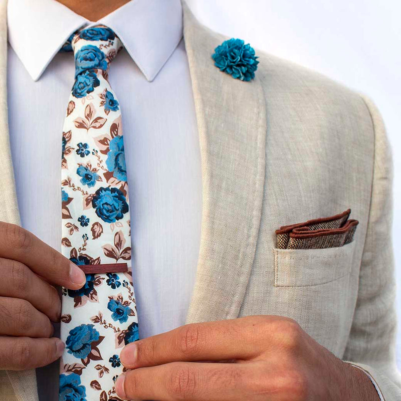 front angle of chicory men's accessories set on linen blazer -  The earthy, wood tie bar along with the wool pocket square give rise to the bright, light blue flowers on the lapel pin and the floral tie