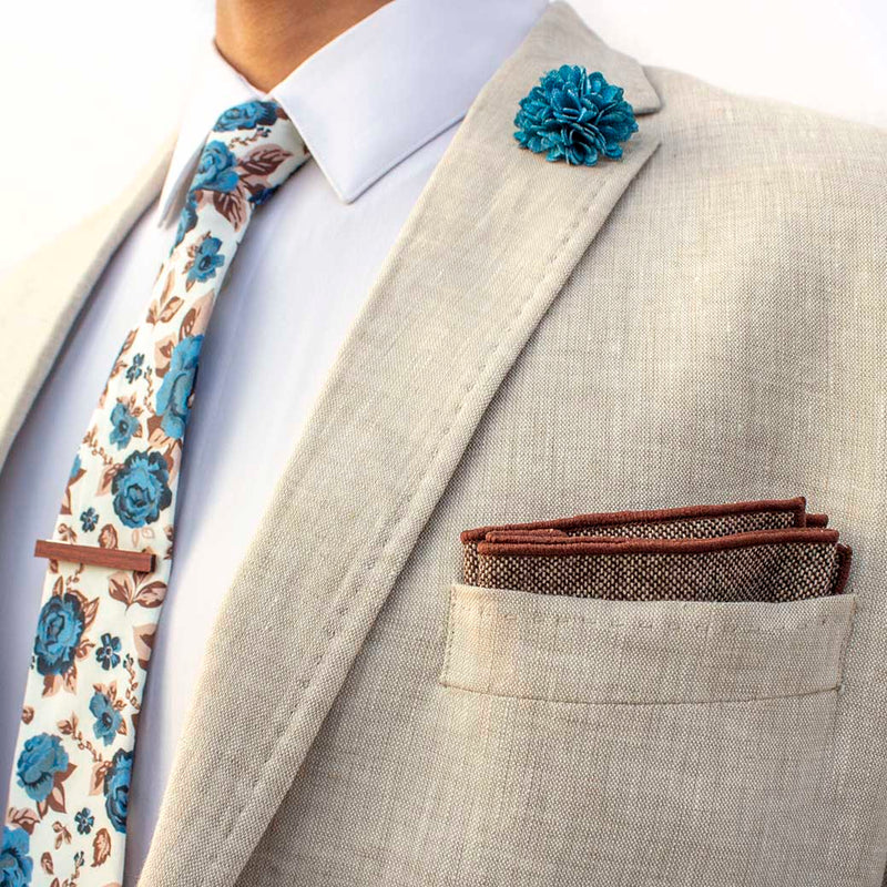 side angle of chicory men's accessories set on linen blazer -  The earthy, wood tie bar along with the wool pocket square give rise to the bright, light blue flowers on the lapel pin and the floral tie
