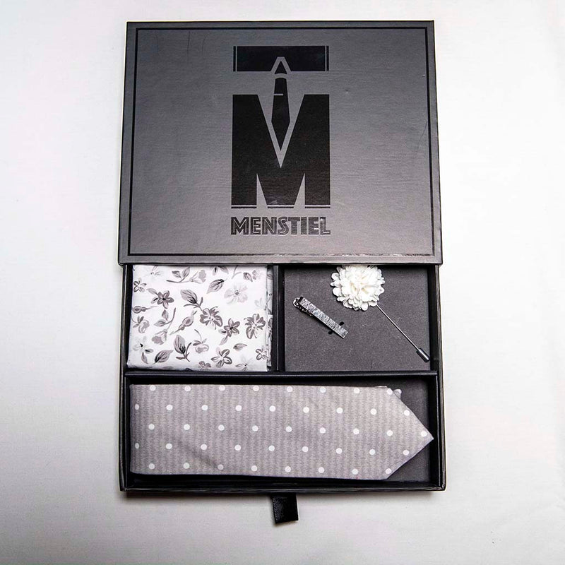 top view of menstiel's distorted set of men's suit accessories in gift box - A solid white lapel flower with a light floral design on the cotton pocket square is just a start. The grey cotton tie incorporates white polka dots over gray reverbs, and is held together by a fractured glass tie bar.