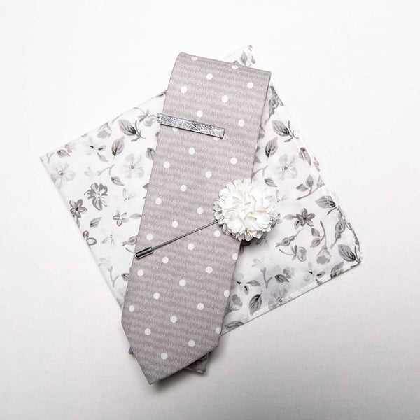 top view of menstiel's distorted set of men's suit accessories - A solid white lapel flower with a light floral design on the cotton pocket square is just a start. The grey cotton tie incorporates white polka dots over gray reverbs, and is held together by a fractured glass tie bar.