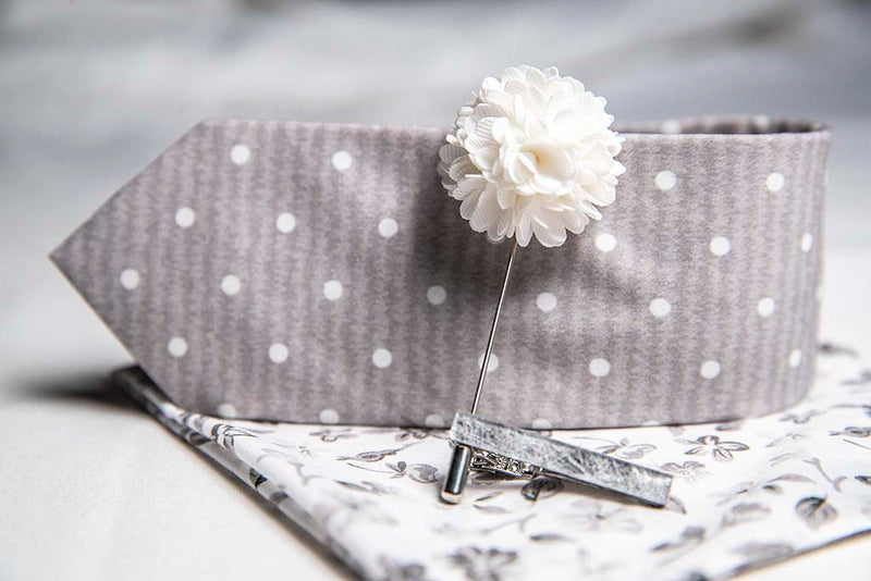 side view of menstiel's distorted set of men's suit accessories - A solid white lapel flower with a light floral design on the cotton pocket square is just a start. The grey cotton tie incorporates white polka dots over gray reverbs, and is held together by a fractured glass tie bar.