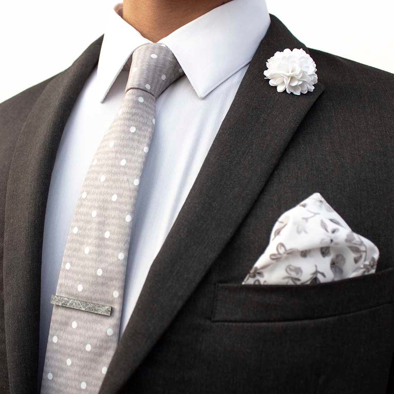side angle of charcoal suit using menstiel's distorted set of men's suit accessories - A solid white lapel flower with a light floral design on the cotton pocket square is just a start. The grey cotton tie incorporates white polka dots over gray reverbs, and is held together by a fractured glass tie bar.