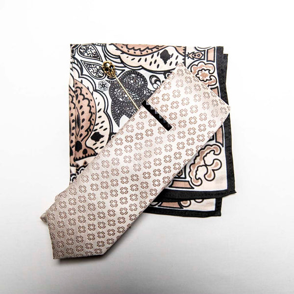 top view of pharaoh set of men's suit accessories - he silk tie’s simple pattern resembling hieroglyphics is a great contrast to the ornamental, paisley silk pocket square, and the black tie bar resembling a sarcophagus is the perfect complement to the gold skull lapel pin of the pharaoh himself