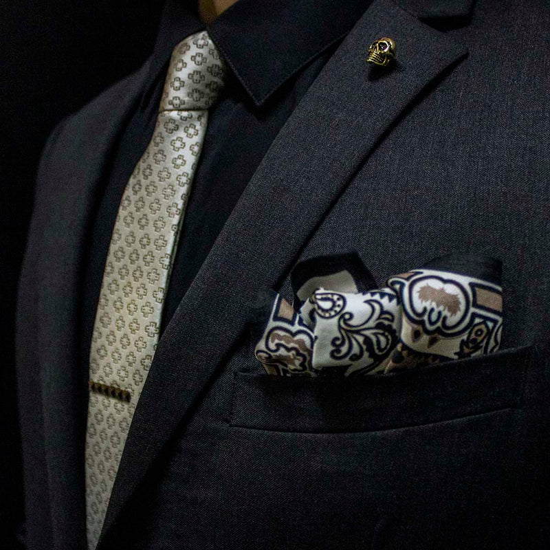 side angle of black charcoal suit with pharaoh set of men's suit accessories - he silk tie’s simple pattern resembling hieroglyphics is a great contrast to the ornamental, paisley silk pocket square, and the black tie bar resembling a sarcophagus is the perfect complement to the gold skull lapel pin of the pharaoh himself