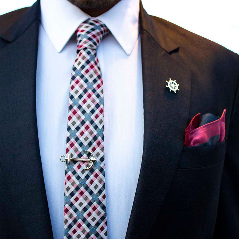 front angle of navy suit using voyage set of men's suit accessories - The silver helm lapel pin on the breast represents choice, while the anchor tie bar on the chest symbolizes strength. These two coupled with the versatile, multi-colored silk tie and silk pocket square make a great combination 