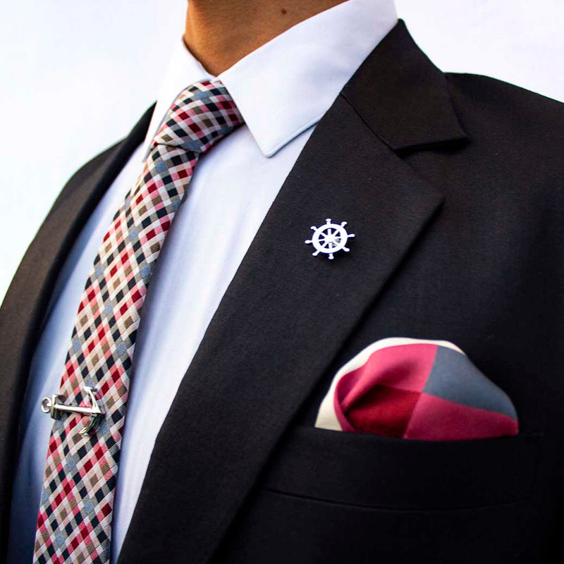 side angle of navy suit using voyage set of men's suit accessories - The silver helm lapel pin on the breast represents choice, while the anchor tie bar on the chest symbolizes strength. These two coupled with the versatile, multi-colored silk tie and silk pocket square make a great combination 